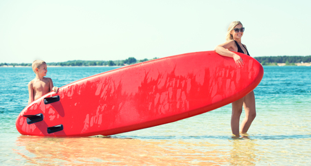 Mother and son stand with apaddle board on the beach of the lake.Water sports, active lifestyle.の写真素材