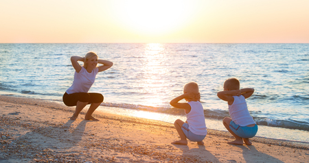 Mother and children do exercises on the beach, they meet the sunrise.Fitness, sport, yoga and healthy lifestyle concept.の写真素材