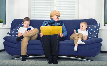 Grandmother reads a book to children, and they play on mobile phones. A social problem.