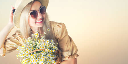 Beautiful woman in hat and with a basket of field daisies in sunny summer day.の写真素材
