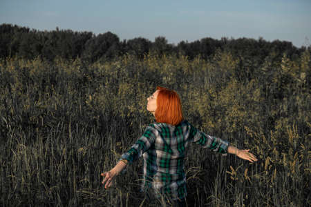 A red haired girl walks through a field of tall grass with her arms open to natureの写真素材