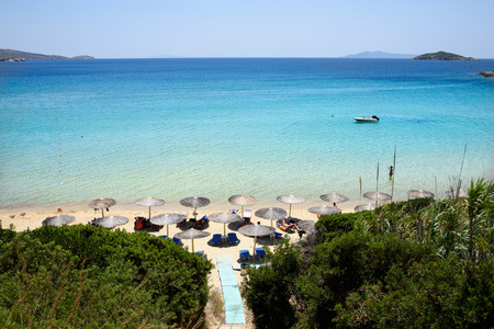 Loungers under palm tree leaves umbrellas on beach in front of crytal clear water.の写真素材
