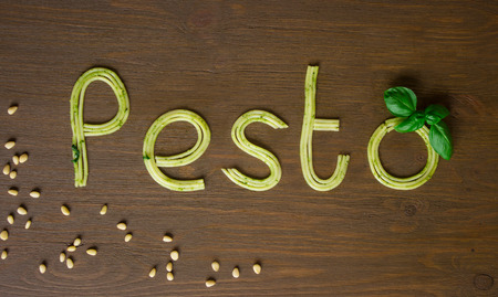 Word pesto made of cooked spaghetti with pesto souce with basil on wooden background