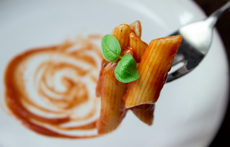 the last piece of penne pasta with tomato sauce on a fork on old wooden tableの写真素材