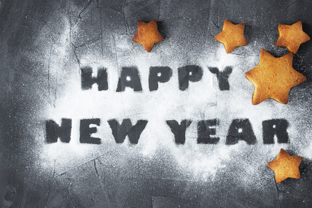 christmas background with baked gingerbread stars and words happy new year made from powdered sugar on the concrete background. creative ideaの写真素材