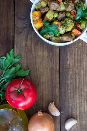 beef meat stewed with potatoes, carrots and spices in ceramic pot with ingredients on wooden background. verticalの写真素材