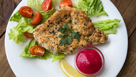 closeup of Homemade Breaded Schnitzel with salad and berry sauce on old wooden table