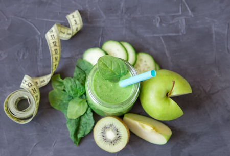 Green smoothie with ingredients: apples, spinach, cucumber and kiwi with measure tape on dark background. healthy eating and dieting conceptの写真素材