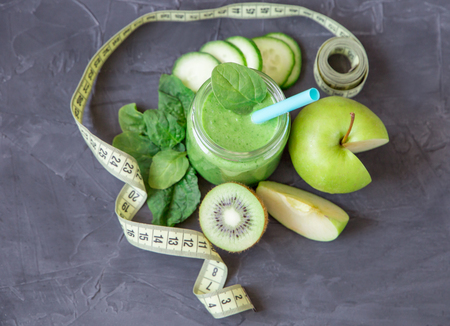 Green smoothie with ingredients: apples, spinach, cucumber and kiwi with measure tape on dark background. healthy eating and dieting conceptの写真素材
