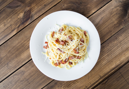 Pasta Carbonara. Spaghetti with bacon and parmesan cheese. Pasta Carbonara on white plate with parmesan on dark background. Italian food concept. Top view.の写真素材