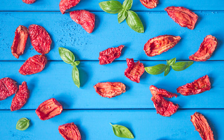 background of sun dried tomato slices with basil leaves on blue wooden table. top viewの写真素材