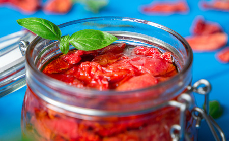 Sun dried tomatoes with basil in a glass jar on a blue wooden table. Traditional recipes of the Mediterranean cuisine. Vegetarian conceptの写真素材