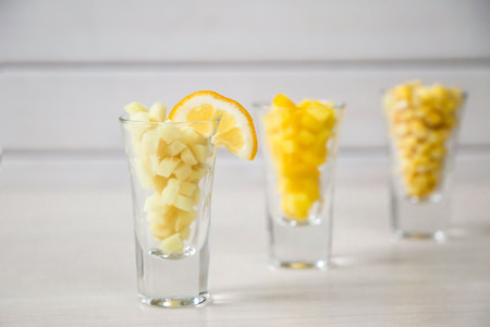 closeup of assortment of yellow cut vegetables in shot glass on white background.の写真素材