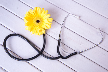 Medical stethoscope with flower on light wooden background. top viewの写真素材