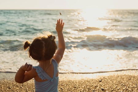 A little girl throws stones at the waves.