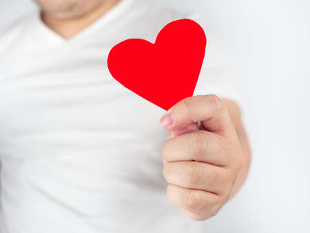 A man in white clothes holding red paper heart Means of love in the month of love valentine's dayの写真素材