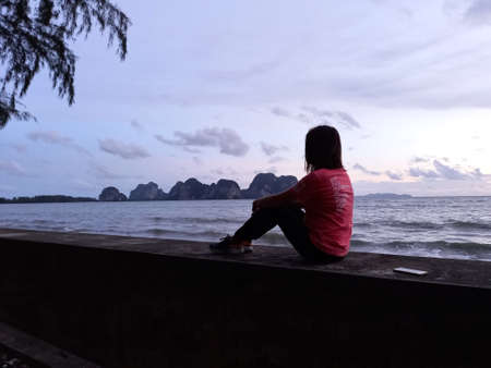 Silhouette of a woman sitting on the bridge and looking at the sea.