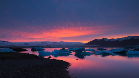 Floating icebergs on JÃ¶kulsÃ¡rlÃ³n glacial lake with black sand beach in foreground  and glacier and mountain and sunset in the background, Southern Iceland.の写真素材