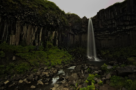 Long exposure of Svartifoss waterfall with its water falling over basalt columns with overcast sky in top. Skaftafell National Park in Southern Iceland.の写真素材