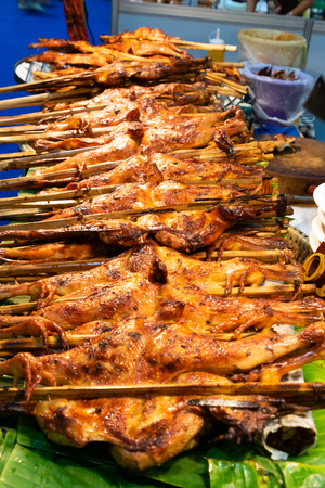 Roasted chicken inserted with bamboo stick and mat with banana leaves.の写真素材