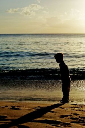 Silhouette of a boy looking at his shadow during a sunset on a beachの写真素材