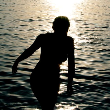 Silhouette of a woman getting out of the ocean with sun setting behind herの写真素材