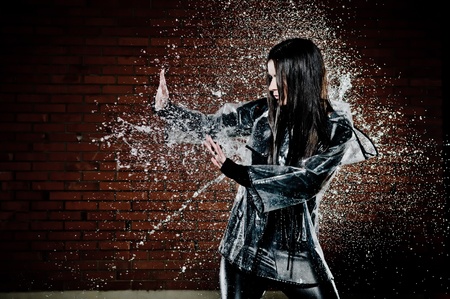 Woman Playing In Rain with water droplets spraying all around her as she tries to ward it off with her hands.の写真素材