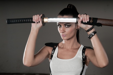 Beautiful woman holding a long shining steel ceremonial sword in front of her headの写真素材