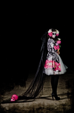 A woman in Halloween costume and skull makeup holding flowersの写真素材