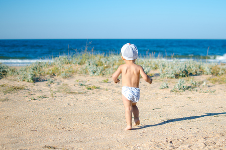 baby in the hat, the shorts, runs to the sea on the sandの写真素材