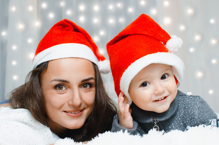 Mother and son very cute beautiful in their red caps lying on the bed behind sparkle garlandの写真素材