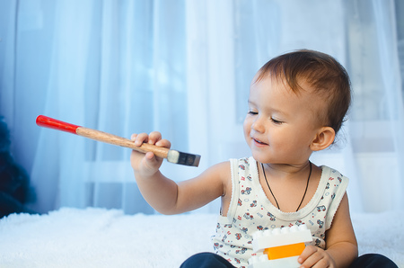 The child is sitting on the bed looking at the hammer holding it in his handsの写真素材