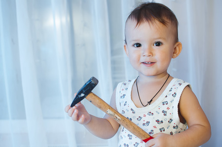 The child sits with a hammer and a screw looking at their toolsの写真素材