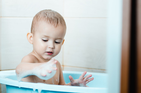 Beautiful boy bathing a toddler in the tub clean and hygienic,looks at the hand which in the foam