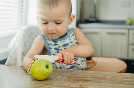 A little boy cuts an Apple using a kitchen knifeの写真素材