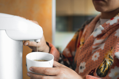 The girl pours water into a mug from the jug in his Bathrobe at homeの写真素材