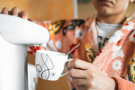 The girl pours water into a mug from the jug in his Bathrobe at homeの写真素材
