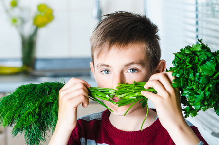 the child in the kitchen with herbs dill and parsley, covering her face like a mustacheの写真素材