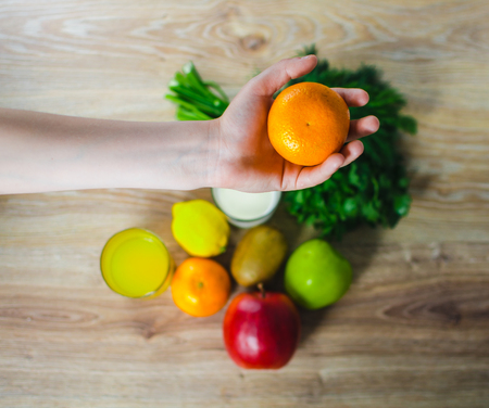 In the hand of the Mandarin, on the background of the table with fruits and greensの写真素材