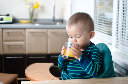baby in the kitchen drinking orange juice, vitamins and healthの写真素材