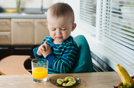 the child in the kitchen with the orange juice and kiwi, healthy,cute and beautifulの写真素材