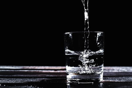 Water in a glass, isolated on a black background with splashesの写真素材