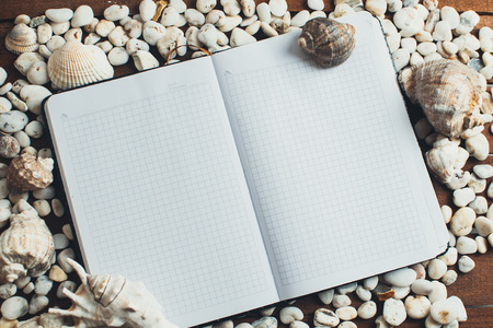 Travel and leisure, on a wooden table is a notebook next to scattered seashellsの写真素材