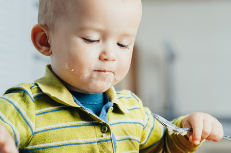 The child in the kitchen alone with a spoon eats mashed potatoesの写真素材