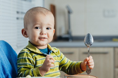 The child in the kitchen alone with a spoon eats mashed potatoesの写真素材