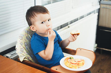 The little boy in the kitchen eating a small pizza, very eagerlyの写真素材
