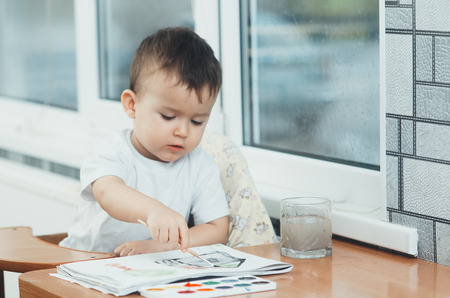 Charming baby in a child seat, draws and paints on paperの写真素材