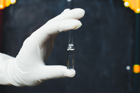 Hand in glove holding a vial against a black backgroundの写真素材
