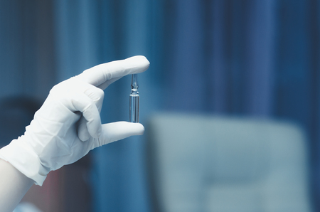 Ampoule in a hand in a glove on a blue backgroundの写真素材