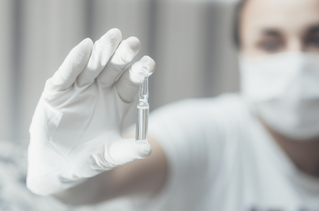 The girl in the mask on the blurred background keeps the vial with a gloved handの写真素材